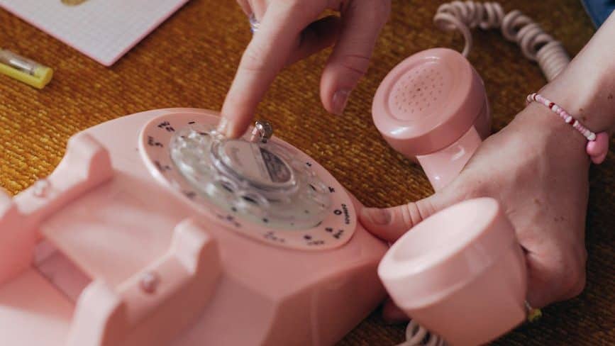 photo of a person s hands using a pink rotary phone