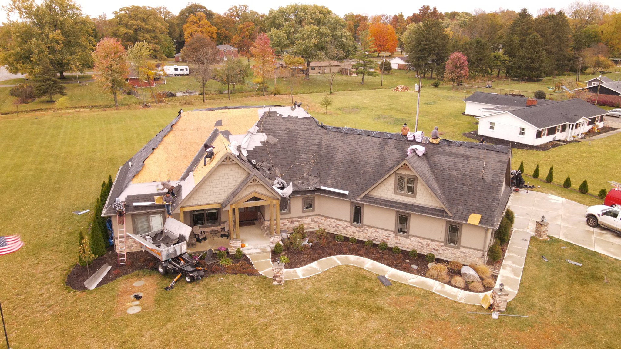 Aerial view of a house undergoing roof replacement, showing roofing contractors installing new shingles, debris removal, and construction tools, highlighting roofing services by Elevated Roofing and Siding.