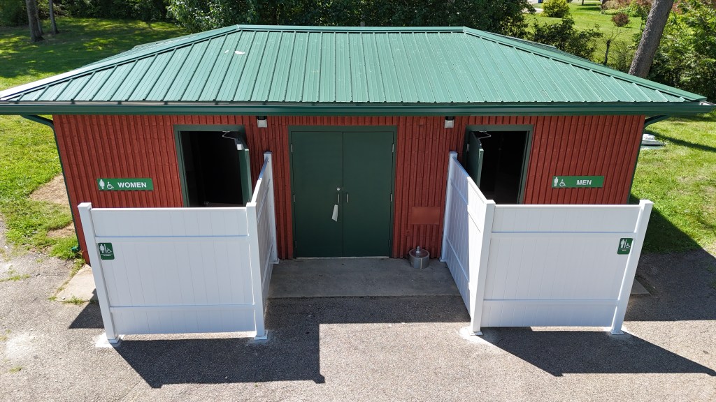 Modern public restroom building with durable metal roofing, red siding, and accessible stalls, showcasing expert roofing and siding installation services.