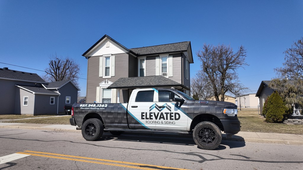 Modern gray siding house featuring upgraded roofing, with Elevated Roofing and Siding service truck parked in the driveway, showcasing professional roofing and siding solutions.