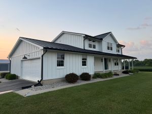 Modern white farmhouse-style home with black metal roofing, vinyl siding, and a manicured lawn, showcasing expert roofing and siding installation by Elevated Roofing and Siding.