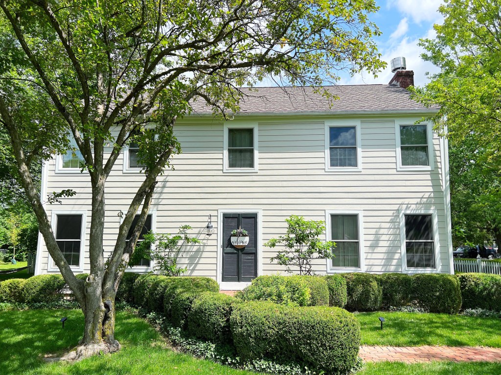 Bright white siding on a well-maintained house with lush landscaping and mature trees, showcasing quality exterior siding and roofing services by Elevated Roofing and Siding.