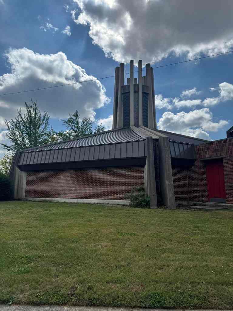 Metal roofing and brick siding on a church building with a tall steeple under a partly cloudy sky.
