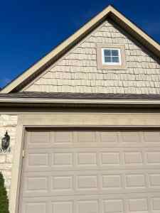 Durable residential shake siding on gable, modern garage door, and exterior wall accents; expert roofing and siding services for home enhancement.