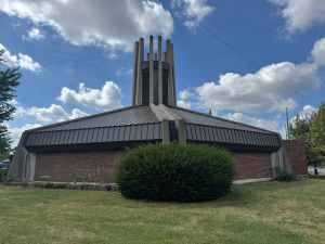 Modern church building with metal roofing, brick walls, and a tall steeple, showcasing professional roofing and siding services.