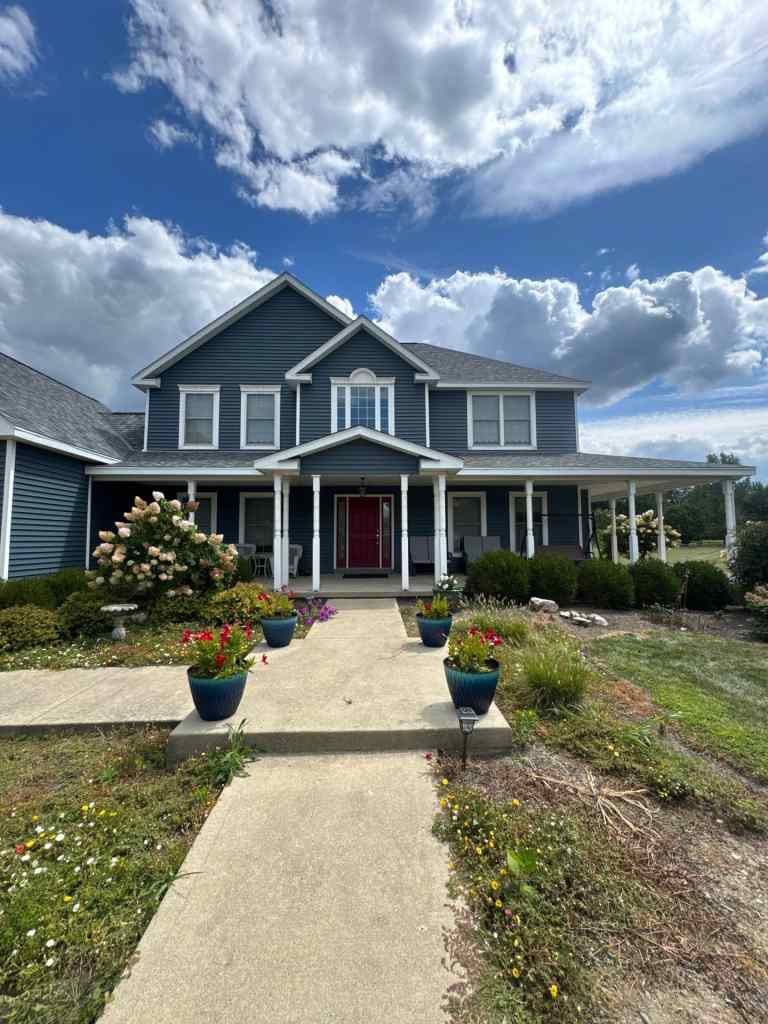 Beautiful blue house with fresh roofing and siding, surrounded by vibrant flowers and lush landscaping. Perfect for home improvement and exterior renovation projects.