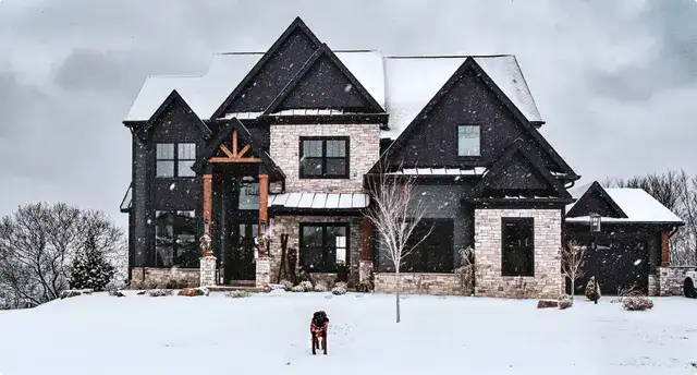 Modern black and white siding with durable roofing on a luxury home during winter snowfall.