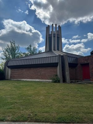 Metal roofing and brick siding on a church building with a tall steeple under a partly cloudy sky.