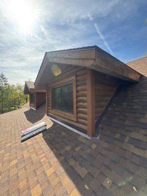 Newly installed roof with asphalt shingles and wooden dormer on a residential house, showcasing roofing and siding repair services.
