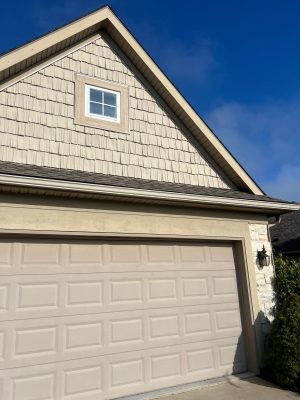 Residential vinyl shake siding and garage door, featuring shingle roof, exterior wall lighting, and corner stone accents, showcasing professional roofing and siding installation.