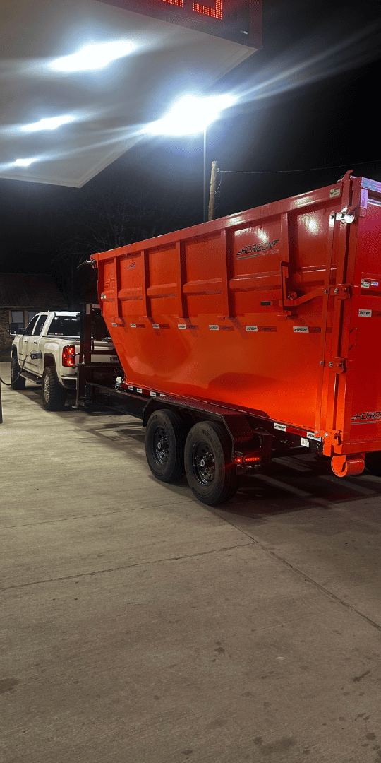Brightly lit red dumpster truck for waste removal at night.