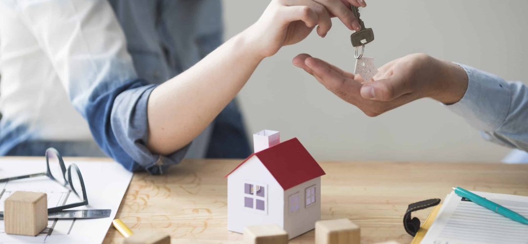 close-up-woman-s-hand-giving-house-key-man-wooden-table