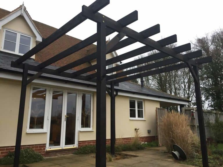 Black wooden garden pergola with beams in Suffolk garden setting.