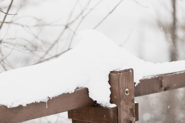 Snow-covered wooden garden fence in winter with snow on top.