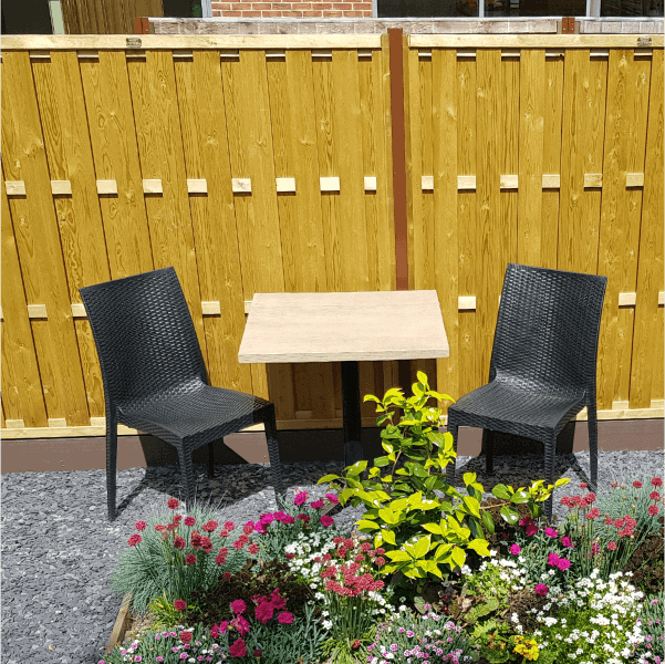 Outdoor garden with table, two chairs, and colourful flower bed.