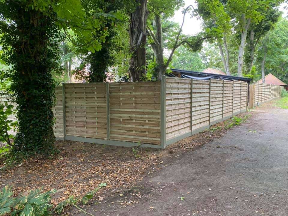 New wooden garden fence with durapost posts and green trees in background.