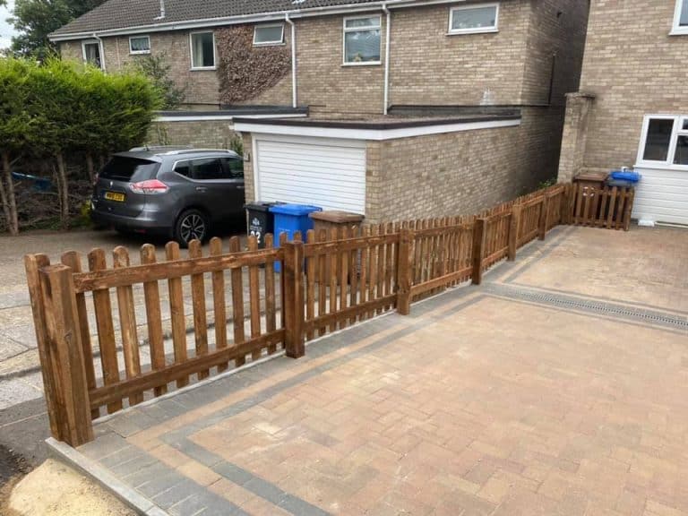 Wooden picket fence installed in a residential driveway area.