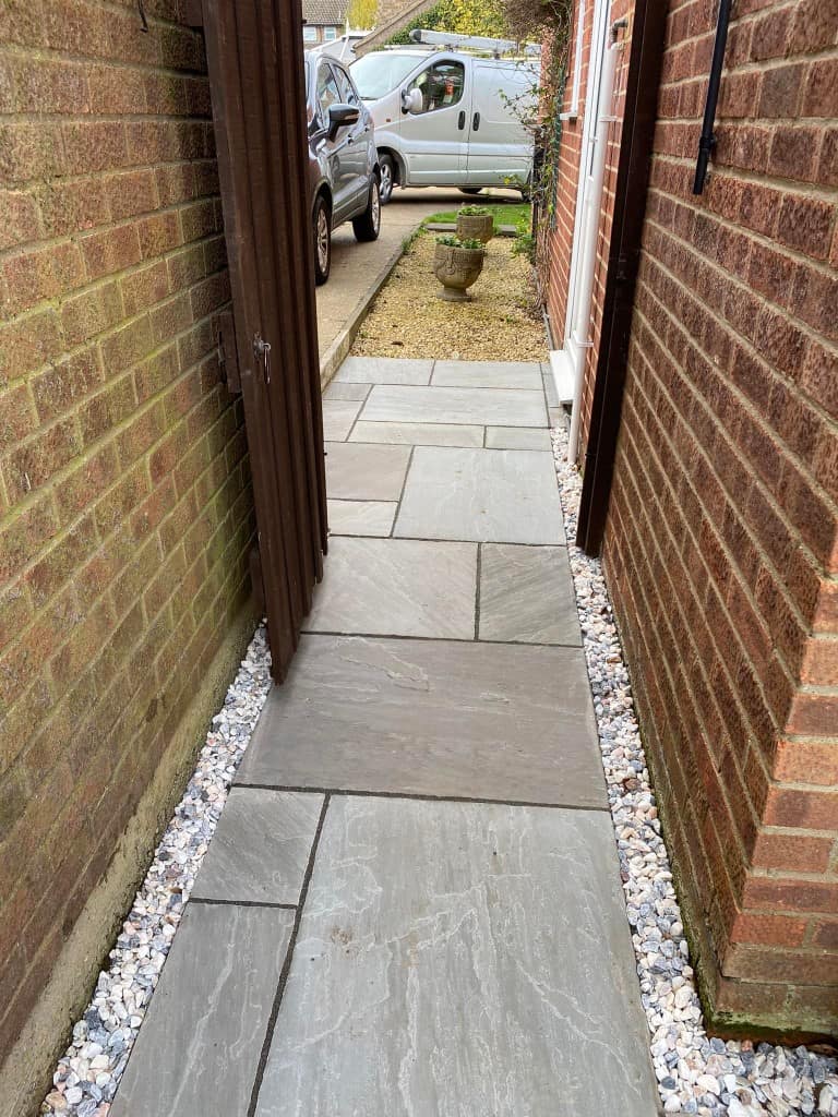 Garden pathway with paving stones between brick walls and a wooden gate.