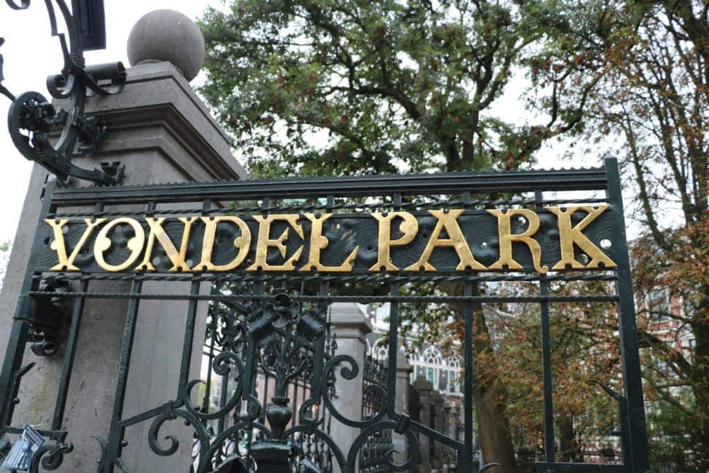 An iron gate marking the entrance to Vondelpark. The park's name is written on the gate in gold lettering.