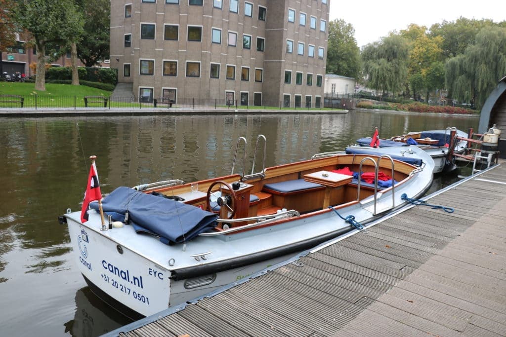 A small white boat is docked at a wooden boarding point on one of Amsterdam's famous canals
