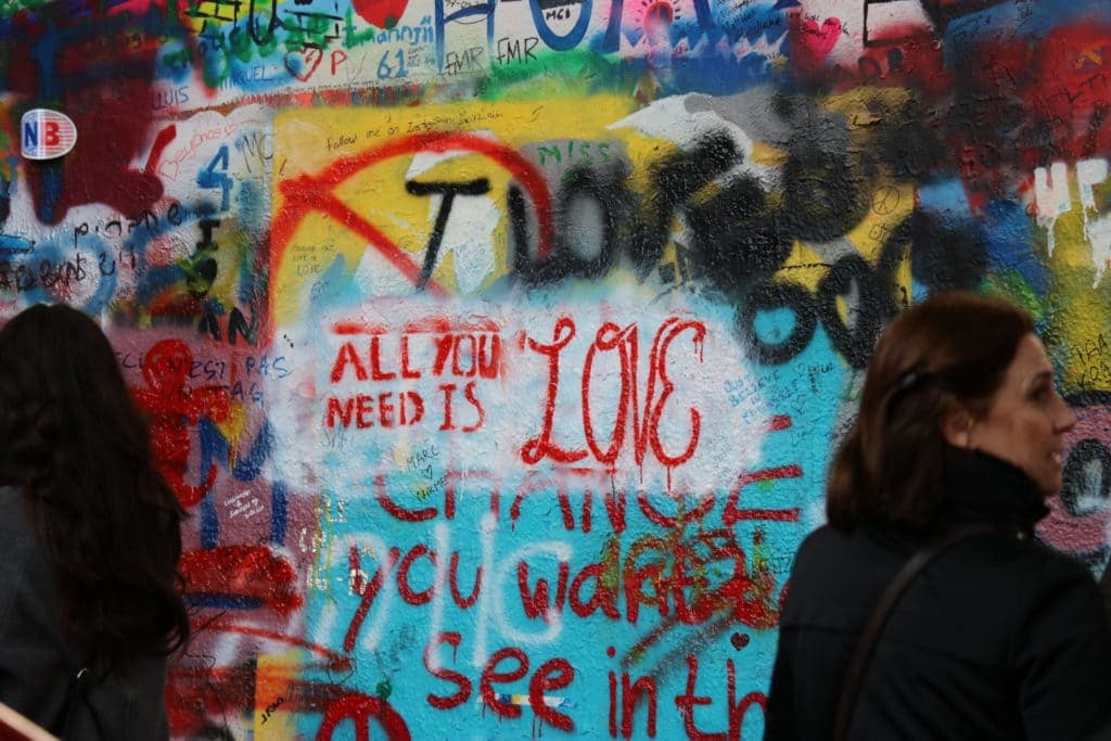 A colourful wall with graffiti and art scrawled on it. In the centre are the lyrics "all you need is love"