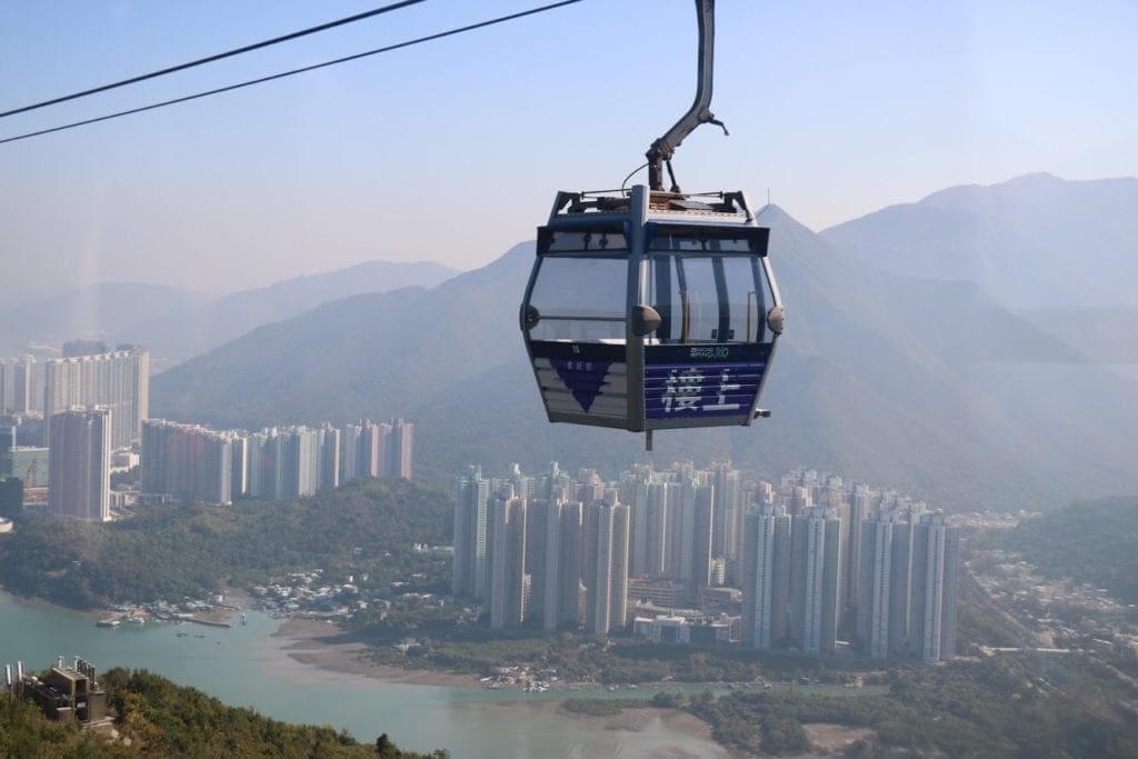 A cable car suspended in the foreground with skyscrapers in the background
