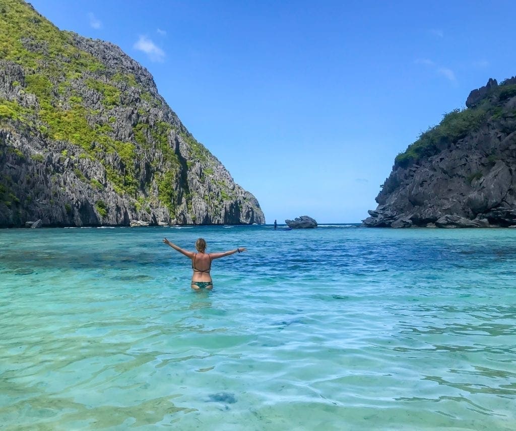 A girl standing waist deep in turquoise ocean, arms outstretched upwards