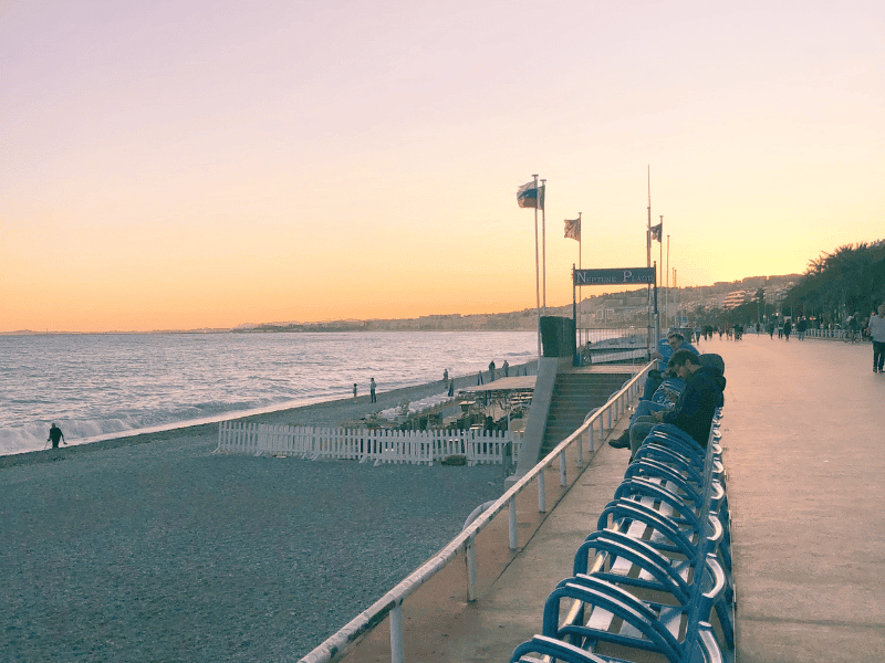 Sunset view along the Nice, France beach promenade with empty chairs and a calm sea, perfect for relaxing and enjoying the scenic coastal atmosphere during golden hour.