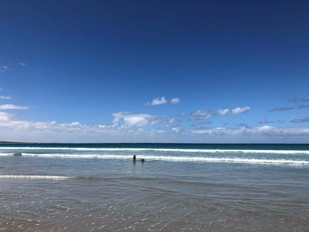Serene beach scene with gentle waves crashing onto the sandy shore under a bright blue sky, perfect for seaside relaxation and ocean exploration in Australia.