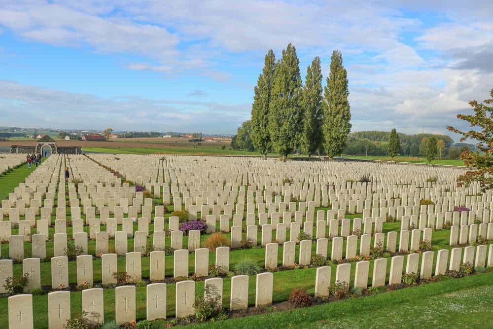 Rows of white gravestones in a memorial cemetery with green grass, tall trees, and a blue sky, part of Emma Jane Explores travel inspiration and sightseeing content in Australia.