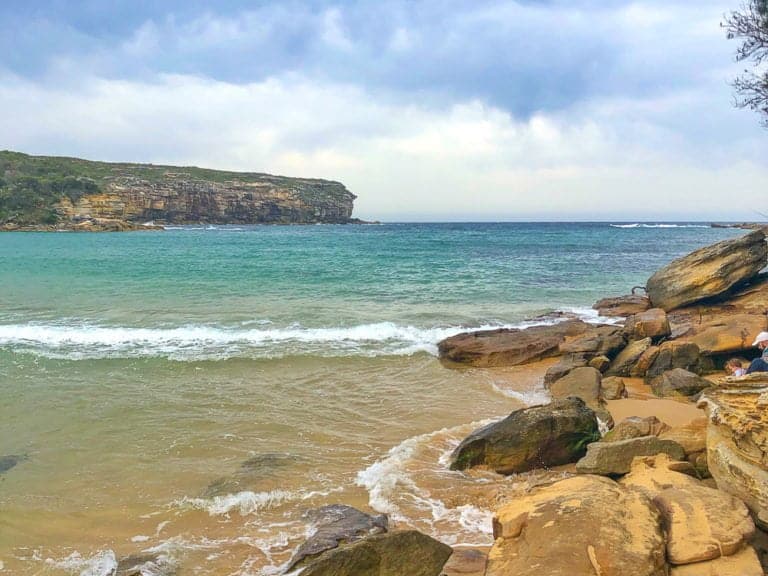 Tranquil coastal beach with rugged rocks, turquoise waters, and scenic cliffs in the background, perfect for exploring and relaxing in nature.