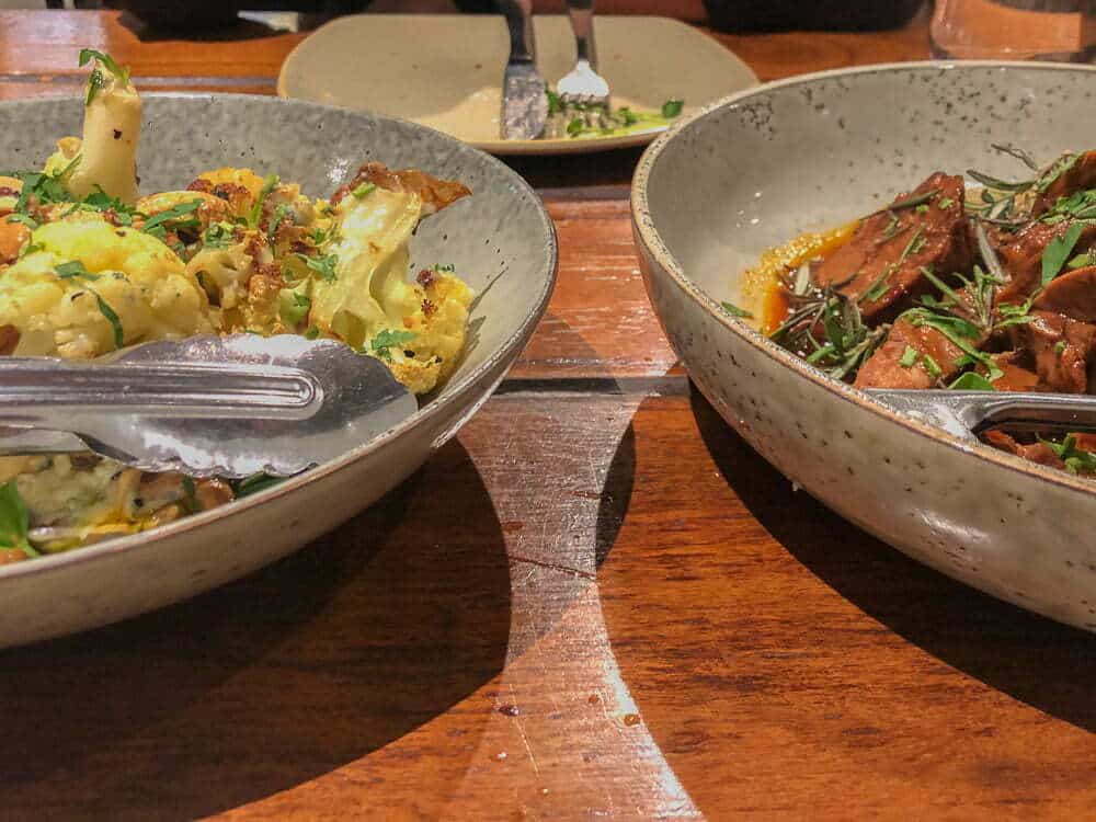 Savory roasted cauliflower and beef dishes served in rustic ceramic bowls at Emma Jane Explores restaurant, highlighting Australian cuisine and dining experiences.