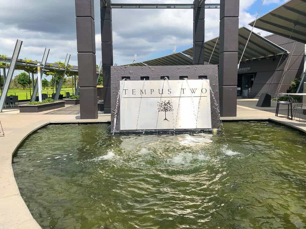 Modern outdoor fountain with "Tempus Two" signage at a wine estate, featuring water features and contemporary architecture, ideal for wine tasting tours and vineyard visits.