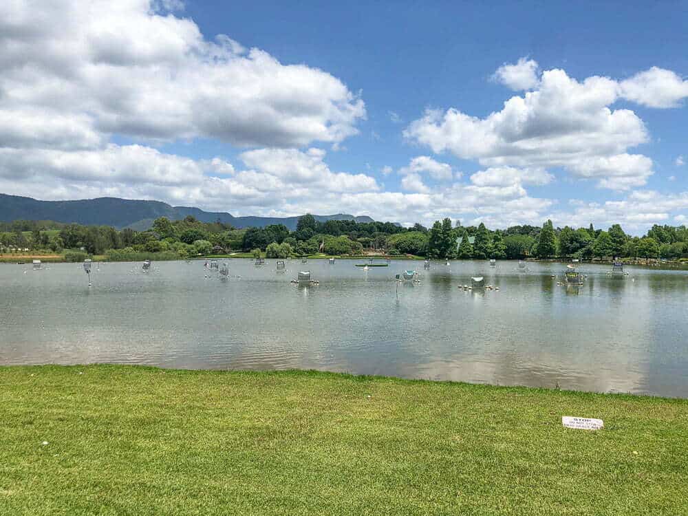 Serene lakeside scene with boats, lush greenery, and mountains under a partly cloudy sky in Australia's outdoor nature destinations.