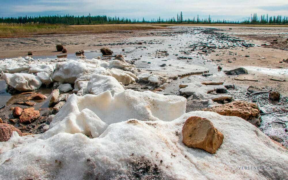 Glacial salt deposits and melting ice on a rugged landscape, in a remote outdoor setting with a distant tree-lined horizon, showcasing natural mineral formations and environmental conditions in Australia.