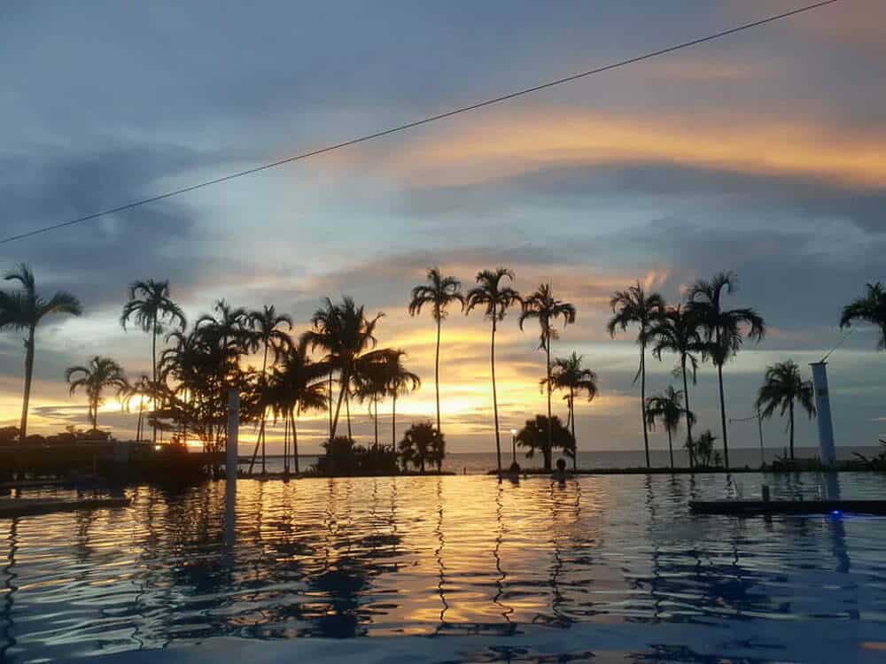 Sunset over palm trees by swimming pool at tropical beach resort, beautiful evening scenery in Australia.