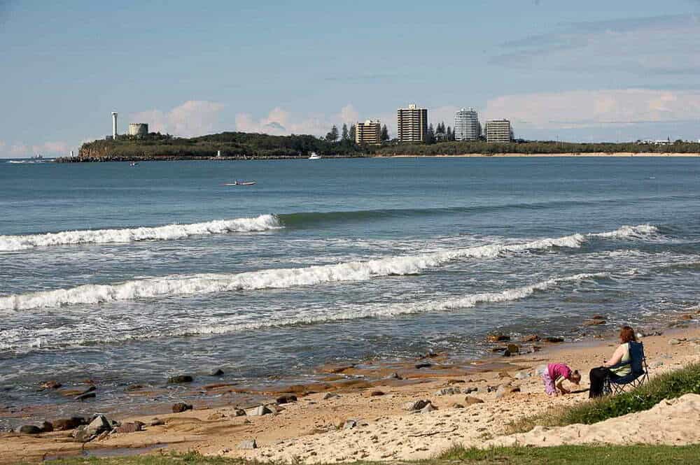 Relaxing woman and child enjoying the beach, ocean waves and city skyline in the background on a sunny day in Australia.