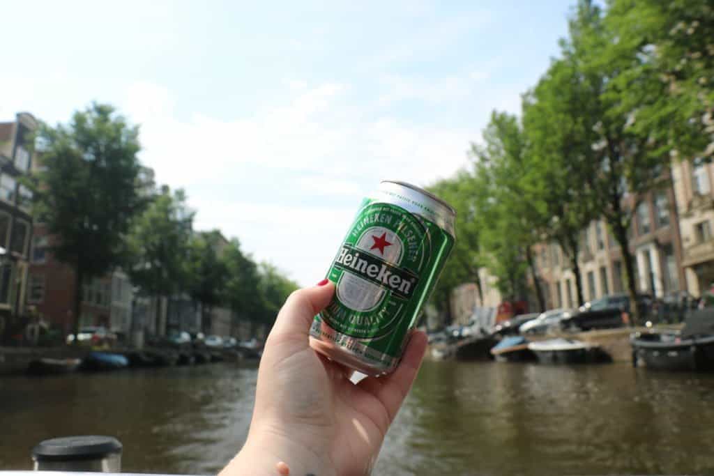 My hand holding a can of Heineken with the canals of Amsterdam in the background