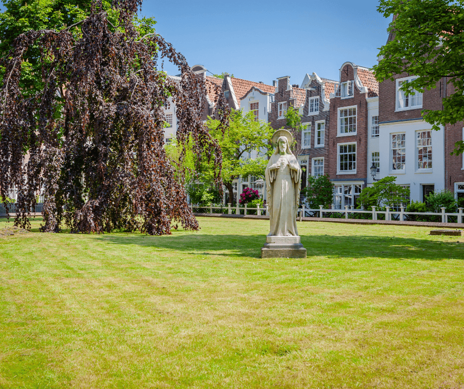 A statue of a haloed Jesus on a green lawn in the Begijnhof with houses in the background