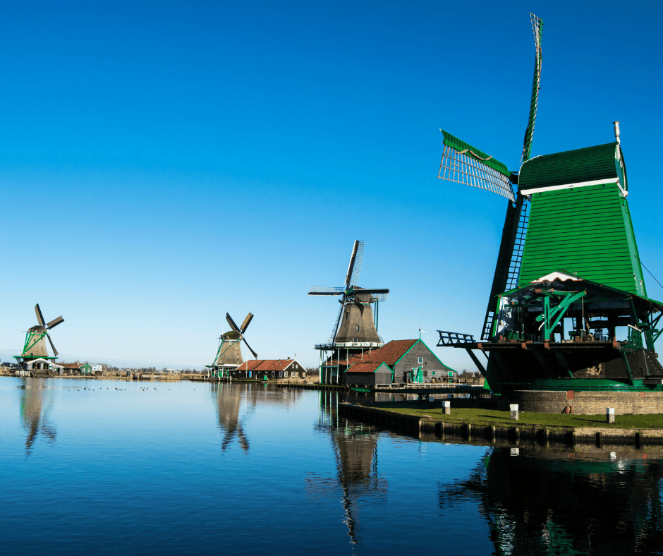 A mirror-still river with green windmills lining the banks. The sky is blue and reflected in the water.