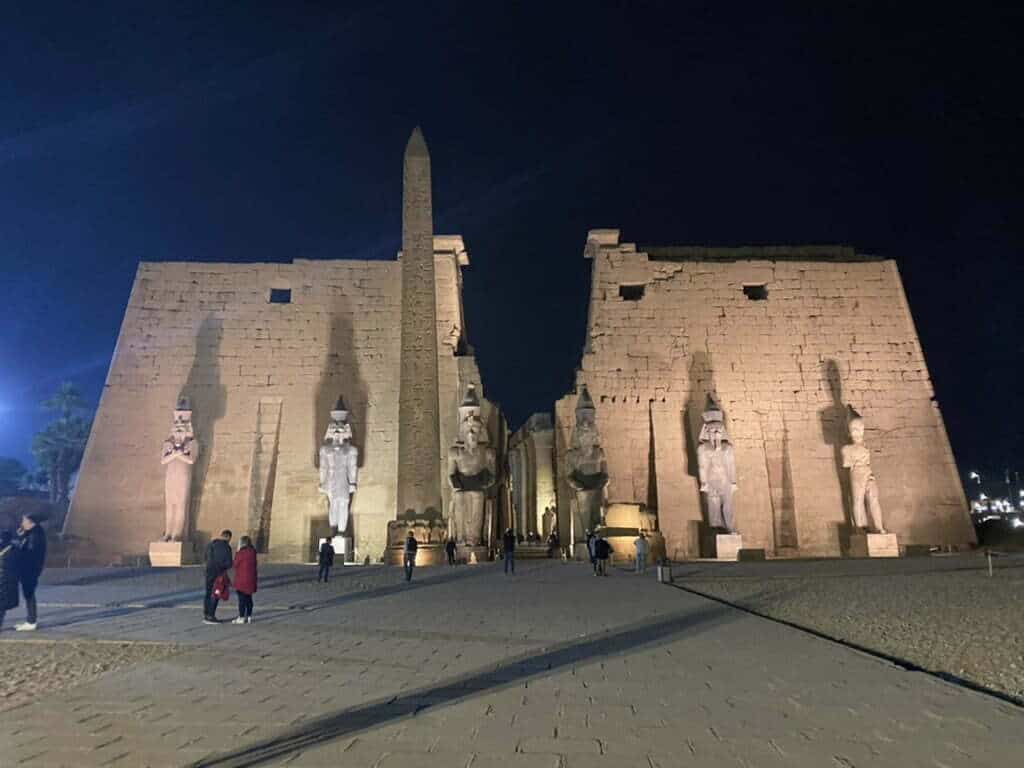 A night time view of the large temples of Luxor with carved statues at the front of the complex.