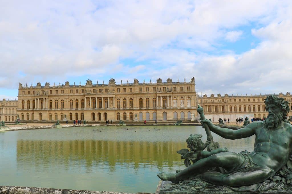 A statue of a bearded man lies in front of a man-made pond with the grand palace building in the background