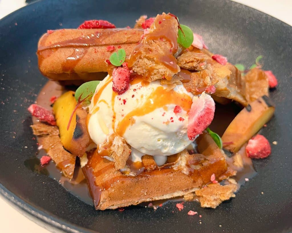 A bowl full of belgian waffle, vanilla icecream and raspberry garnish from Crack Kitchen