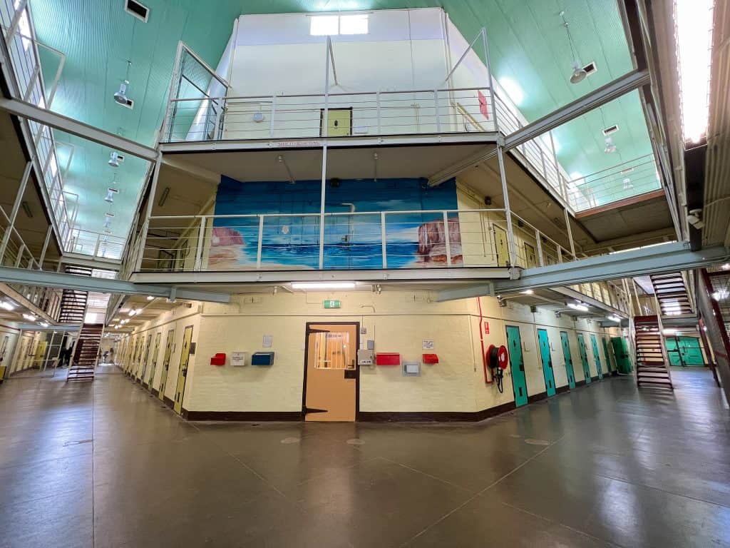 A large cream coloured two-story cell block with a large mural painted on the upper level.