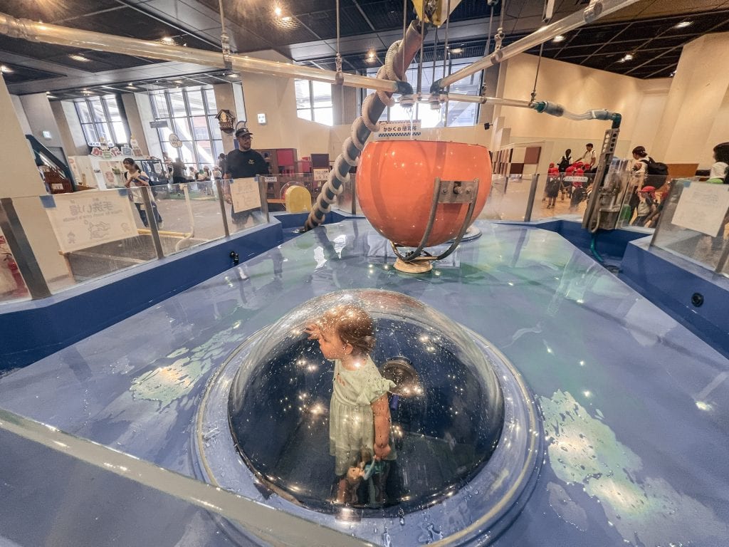 The water play station at Osaka Kids Plaza. A small girl stands in the centre of the photo.