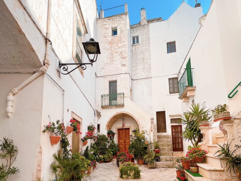 Quaint Mediterranean alleyway with whitewashed walls, vibrant potted plants, and rustic charm, perfect for exploring traditional Italian architecture and colourful outdoor decor.