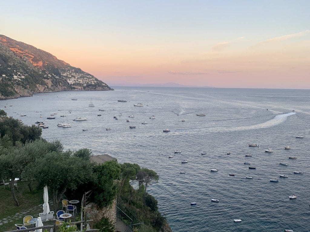 Scenic view of a harbour with numerous boats and yachts at sunset, surrounded by lush green hills and a serene sky, perfect for exploring stunning coastal destinations in Italy.