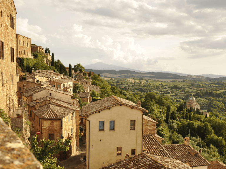 Charming hillside Italian village with rustic stone buildings and terracotta rooftops overlooking lush green countryside and rolling hills.