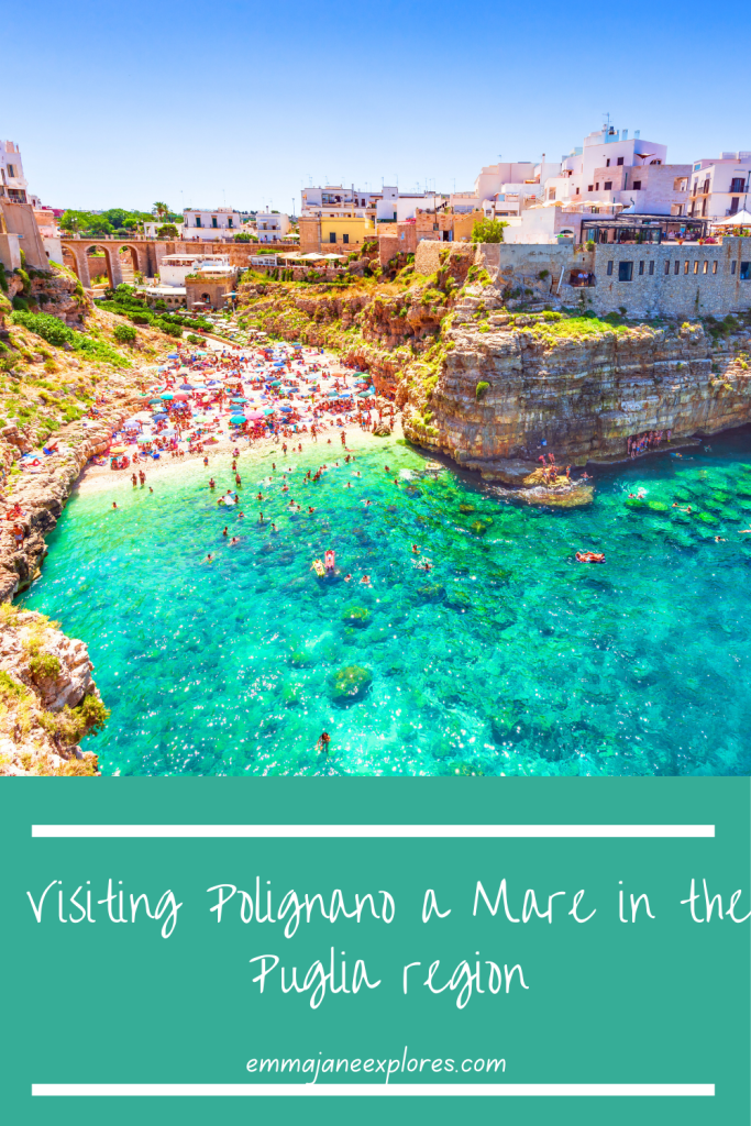 Crystal-clear coastal waters with a lively beach scene at Polignano a Mare in the Puglia region, featuring cliffs, colorful umbrellas, and historic white buildings under a bright blue sky.
