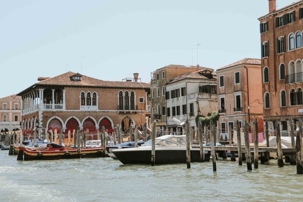 Colourful Venetian buildings along a canal with boats and wooden piers in Venice, Italy.